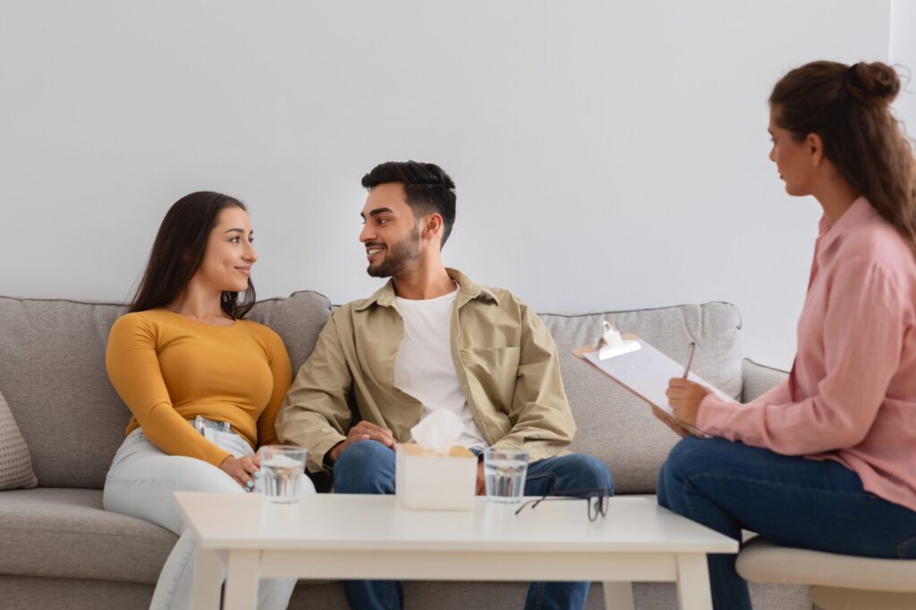A couple sitting across from a therapist during marriage counseling, looking hopeful and engaged in conversation